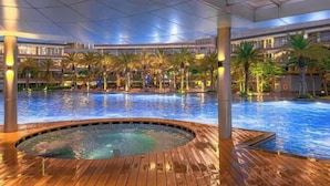 Una amplia piscina interior con jacuzzi, rodeada de palmeras y arquitectura moderna.