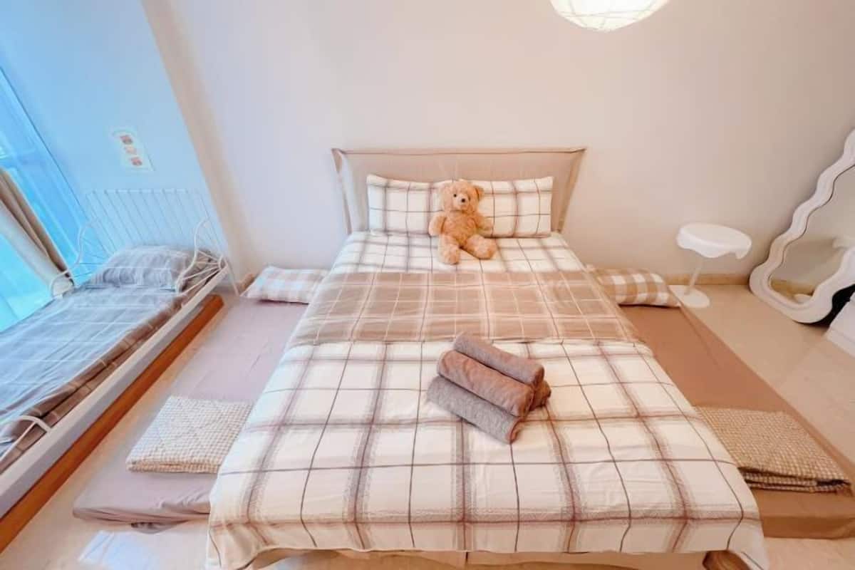 Een slaapkamer met een bed, nachtkastje, spiegel en een teddybeer.