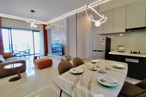 A modern living room with a sofa, a dining table set with plates and cutlery, and a kitchen area with cabinets and appliances. - Deluxe 3 Bed 3 Bath Apartment (Johor Bahru)