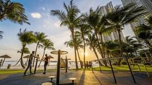A park with exercise equipment, palm trees, and a view of the sea.