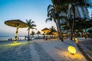 A beachside resort with thatched umbrellas, palm trees, and a sandy walkway.