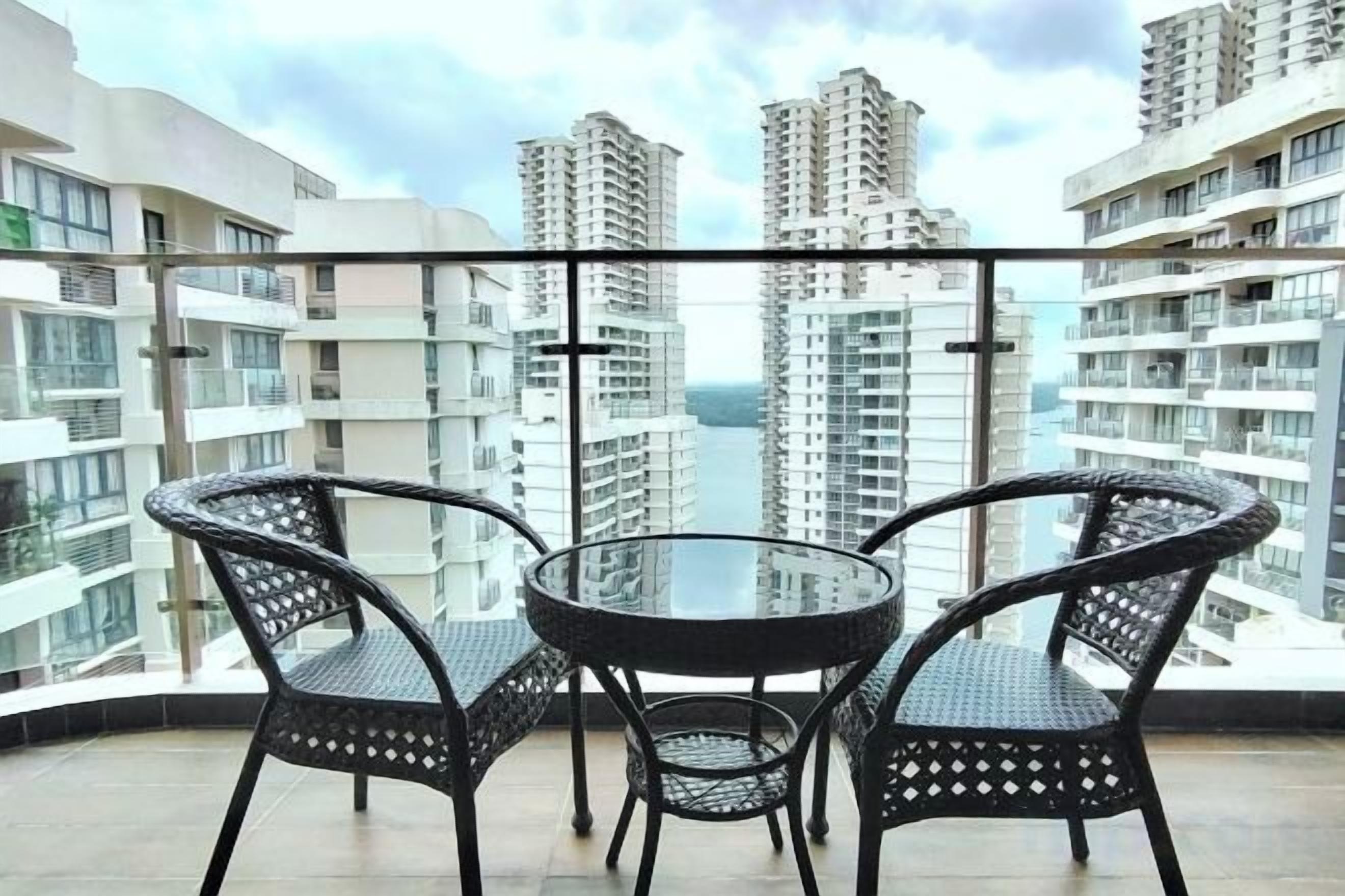A balcony with a round table and two chairs, overlooking high-rise buildings.