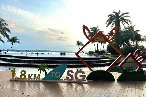 A sign indicating a distance of 18 km to Singapore, with palm trees and a water feature in the background.