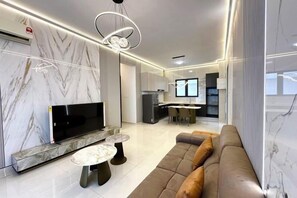 Een moderne woonkamer met een flatscreen televisie, een accentmuur van marmer, een bank en een eethoek op de achtergrond.