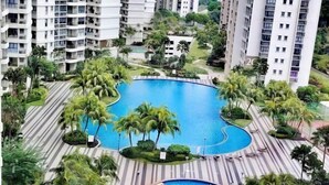 A high-rise residential building with a central swimming pool surrounded by palm trees and a landscaped area.