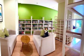 A library with bookshelves, two white sofas with cushions, and a wooden table. - Deluxe 3 Bed 3 Bath Apartment (Johor Bahru)