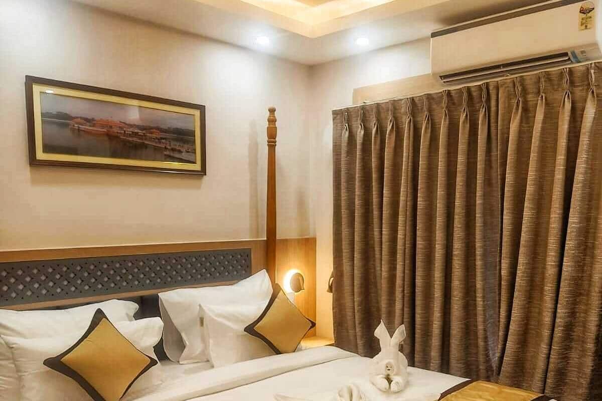 Une chambre d’hôtel avec un lit bien fait, une tête de lit, un climatiseur fixé au mur, un tableau encadré et une fenêtre avec des rideaux.