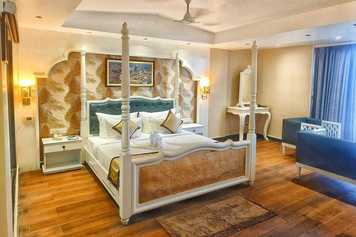 Un lit à baldaquin, une table de chevet, une commode, un canapé bleu et une grande fenêtre avec des rideaux.