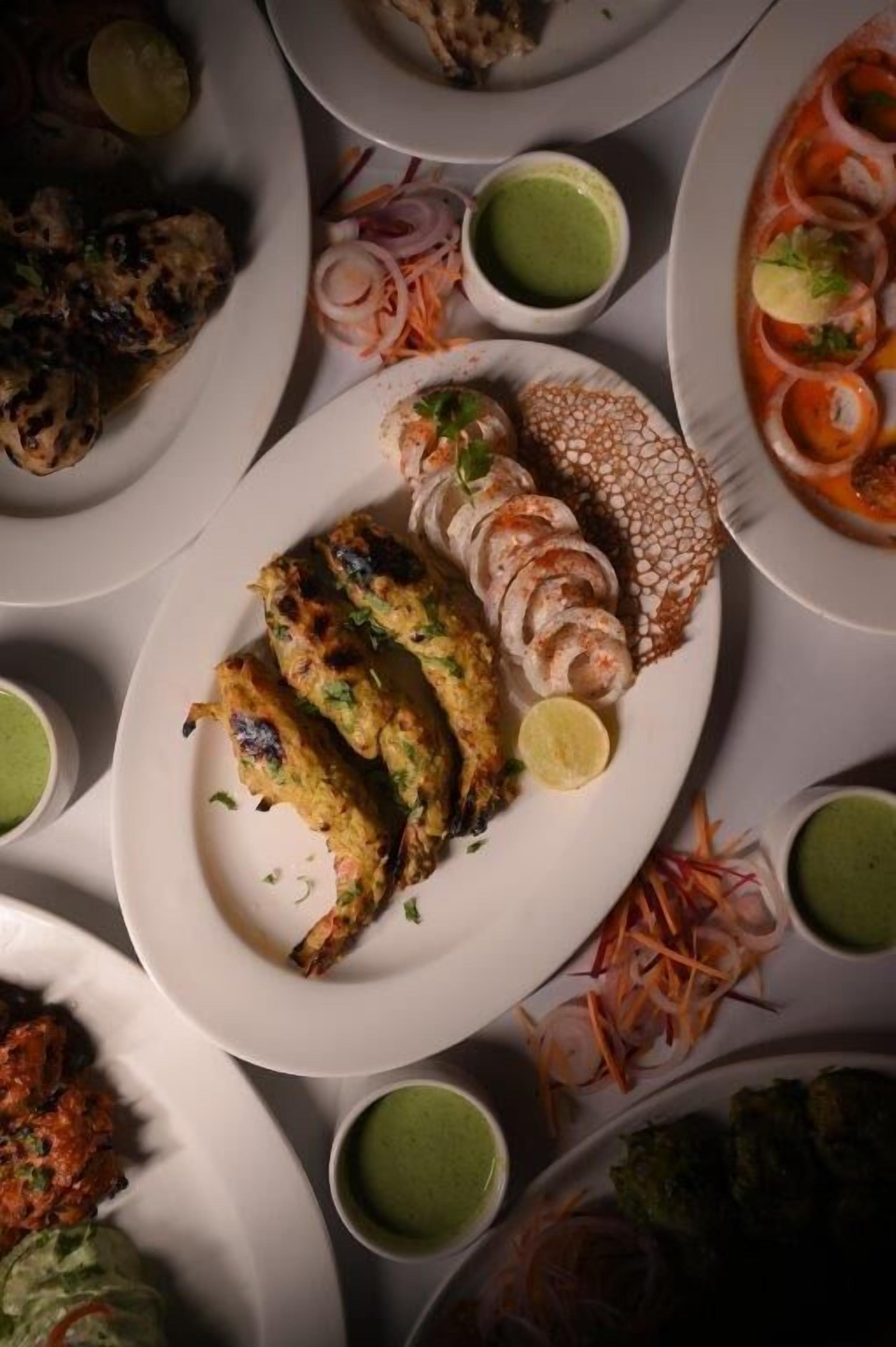 A variety of dishes including grilled chicken, shrimp, and vegetables, served on white plates with green chutney.