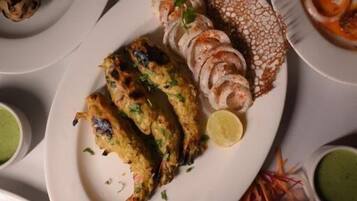 A variety of dishes including grilled chicken, shrimp, and vegetables, served on white plates with green chutney.