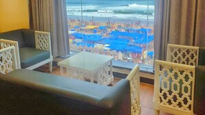Une pièce dotée d’une grande fenêtre donnant sur la plage, et aménagée avec un canapé, des fauteuils et une petite table.