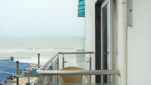 Un balcon doté d'une rambarde en verre, d'un fauteuil en osier et offrant une vue sur la plage.