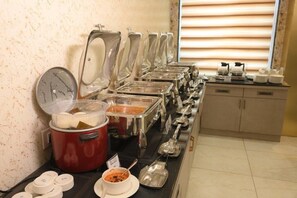 A buffet setup with various food containers and utensils, a red slow cooker, and a window with blinds in the background. - Golden Retreat (Puri)