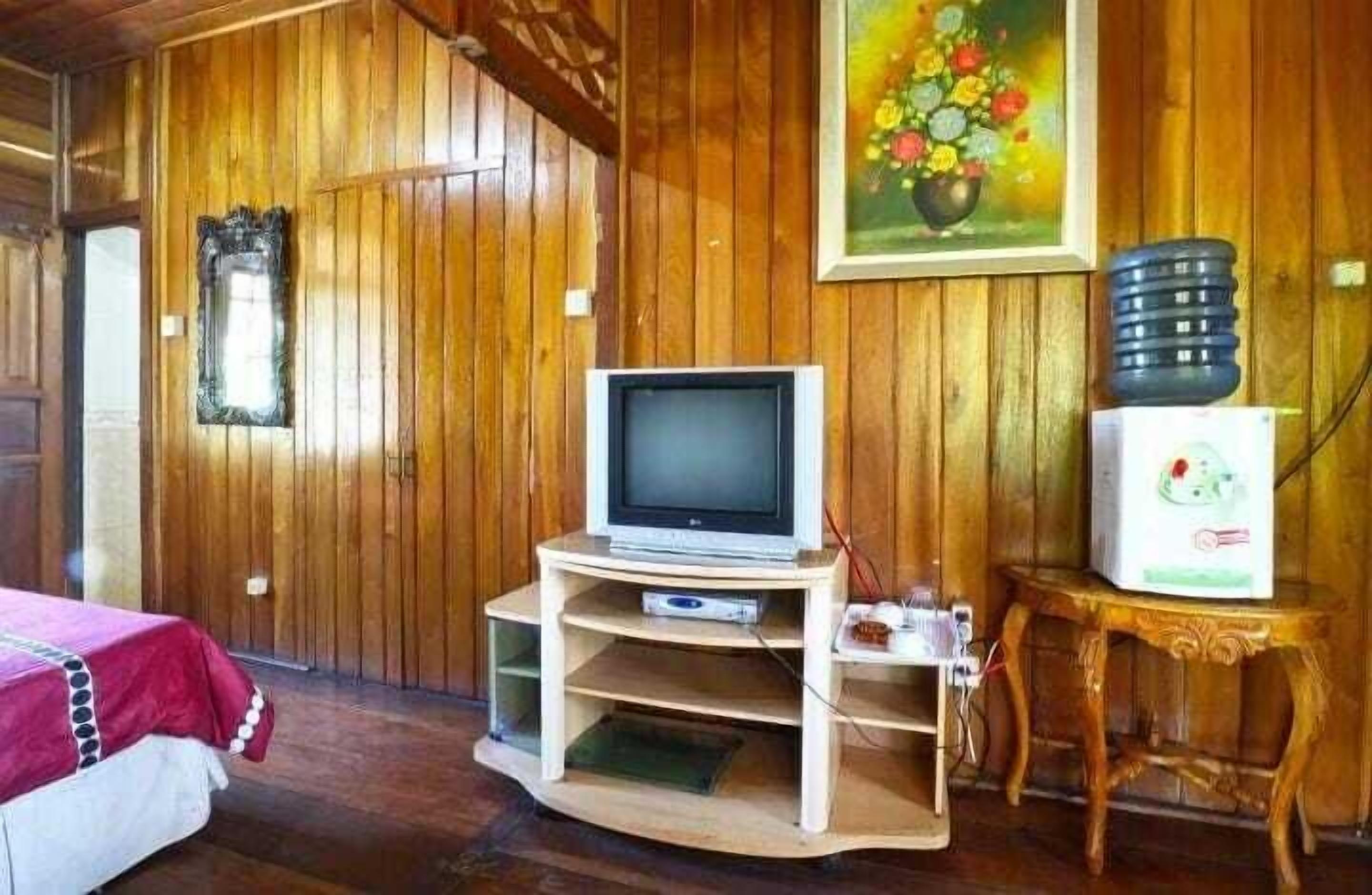 A wooden-paneled room with a television on a wooden stand, a small table with a water dispenser, and a painting on the wall.