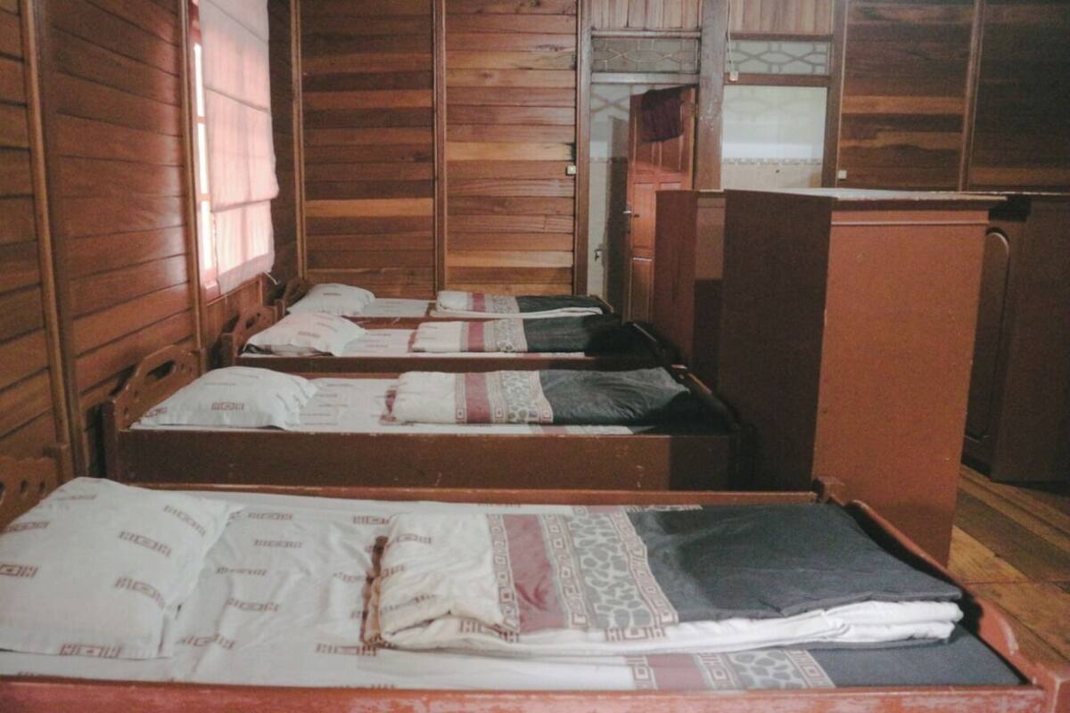 Een kamer met houten wanden en vloeren, met daarin drie houten bedden voorzien van wit beddengoed.