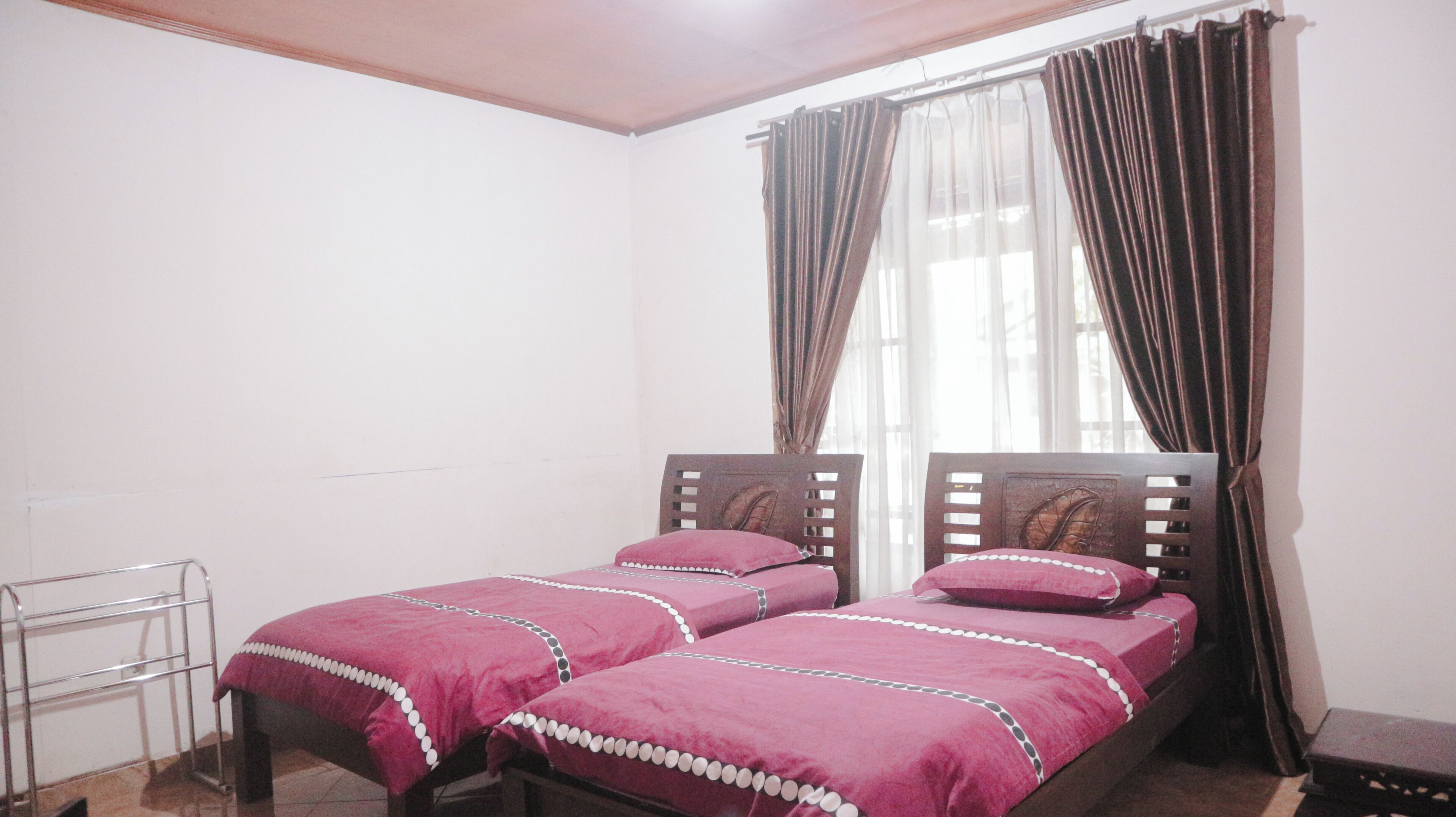 A bedroom with two single beds, a metal chair, and a window with curtains.