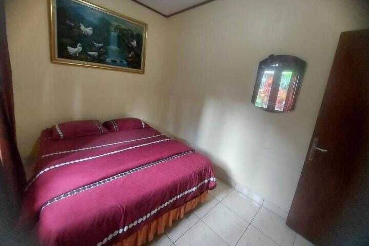 Een slaapkamer met een bed, een schilderij aan de muur en een klein kastje.