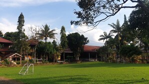 A grassy area with a soccer goal, surrounded by trees and buildings with red roofs. - Aquarius Orange Hotel & Villa (Cisarua)