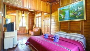 A wooden cabin-style room with a bed, a television, and a painting of a waterfall. - Aquarius Orange Hotel & Villa (Cisarua)
