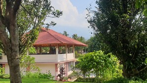 A two-story building with a red-tiled roof, surrounded by lush greenery and trees. - Aquarius Orange Hotel & Villa (Cisarua)