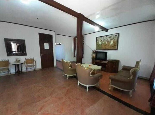 A living room with a television, two armchairs, a small table, and a painting on the wall. - Aquarius Orange Hotel & Villa (Cisarua)