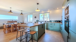 Een moderne keuken met een centraal eiland, barstoelen, een houten eettafel en hanglampen.