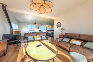 Een ruime woonkamer met een ronde houten tafel, leren banken en een keuken op de achtergrond.