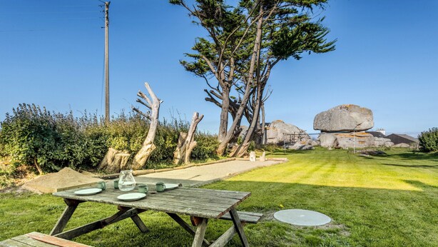 Een picknicktafel met borden en een karaf, omringd door een gazon met bomen en rotsen.