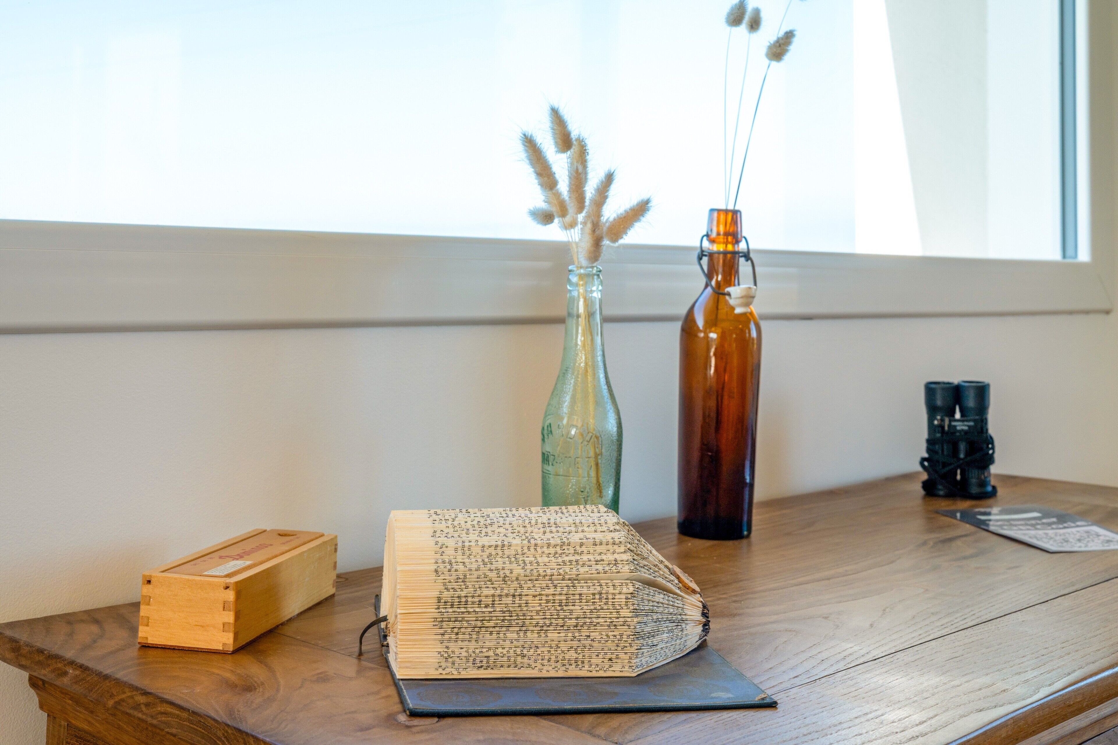 Ein Holztisch mit einem Buch, einer Glasflasche und einem Fernglas.