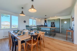 Een moderne keuken met houten vloeren, hanglampen en een eethoek met een tafel voor vier personen.