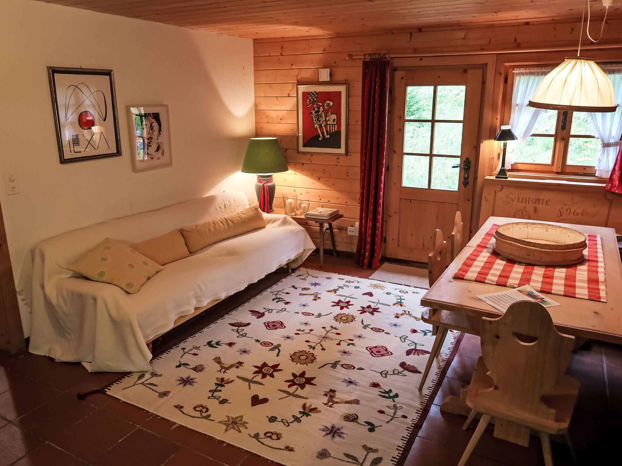 Ein gemütlicher Raum mit Holzbalkendecke, einer Couch, einem Esstisch mit kariertem Tischläufer und einem floralen Teppich.