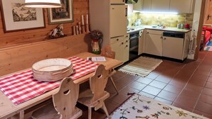 Un interior de madera con una mesa de comedor, sillas, una zona de cocina con armarios, una estufa y un lavamanos.