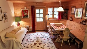 Una habitación acogedora con paredes de madera, una cama, una mesa con sillas y un ventanal con cortinas.