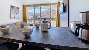 Une cuisine moderne avec une grande fenêtre, une table à manger avec des bols et une bouilloire, et une vue sur les montagnes.