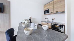 Une cuisine moderne dotée d’un plan de travail en marbre, de meubles en bois, d’un four à micro-ondes, d’une machine à café et d’un coin repas avec une chaise et des bols.