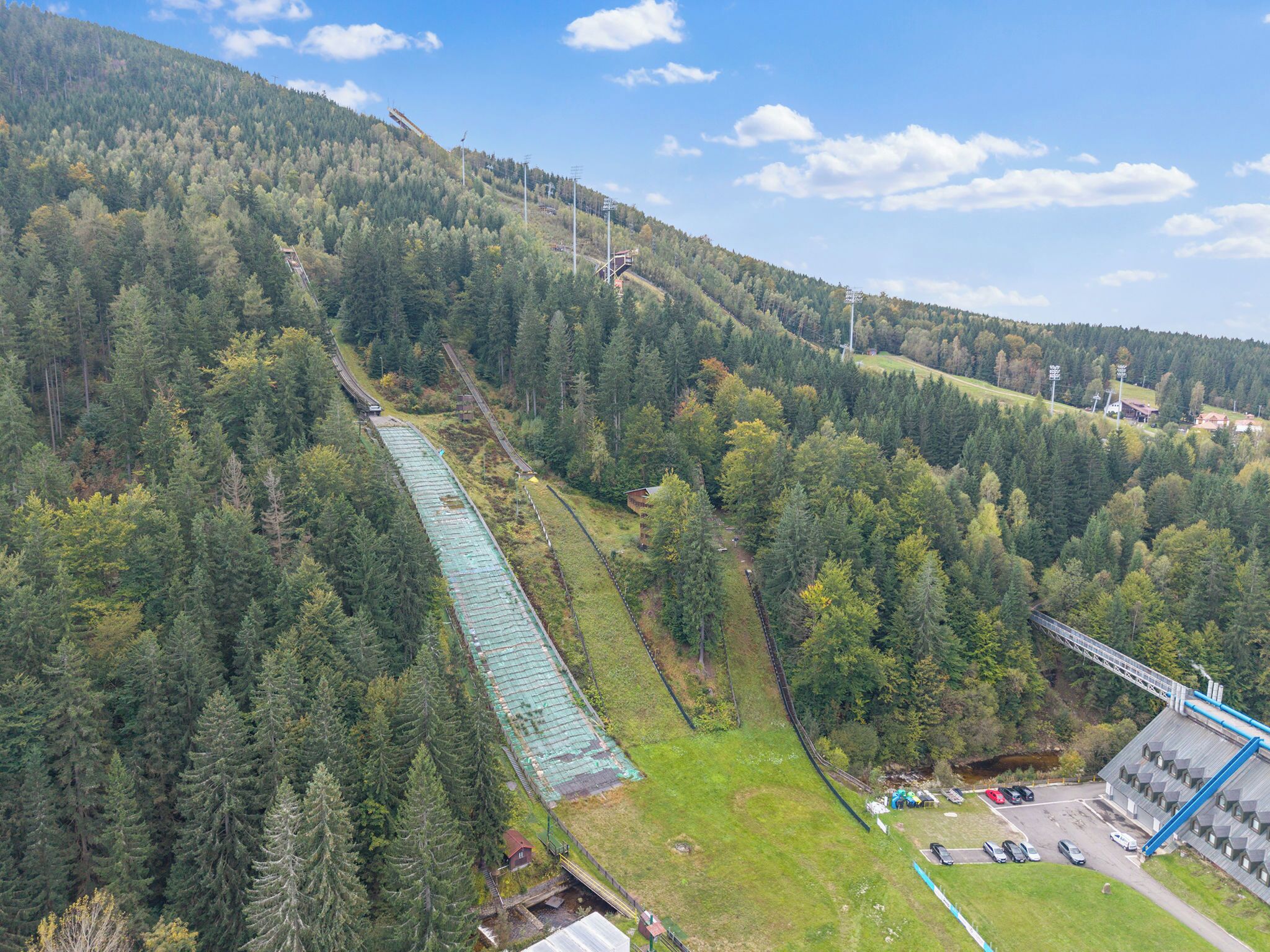 A mountainous area with a green-roofed building, a parking lot, and a bridge.