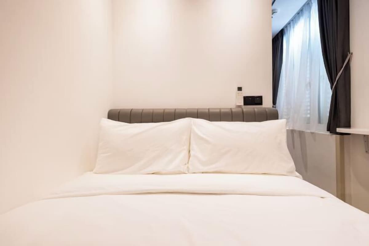 Una cama con ropa blanca, un cabecero y una ventana con cortinas.