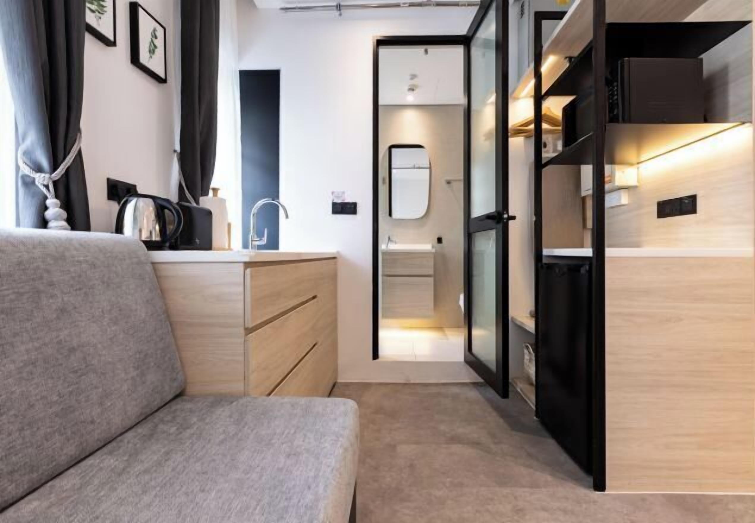 Una habitación moderna con sofá, cómoda de madera, lavamanos y puerta de vidrio que da al baño.