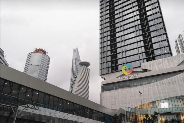 A modern building with a glass facade, a distinctive logo, and a pedestrian bridge. - KL Gateway Residence (Kuala Lumpur)