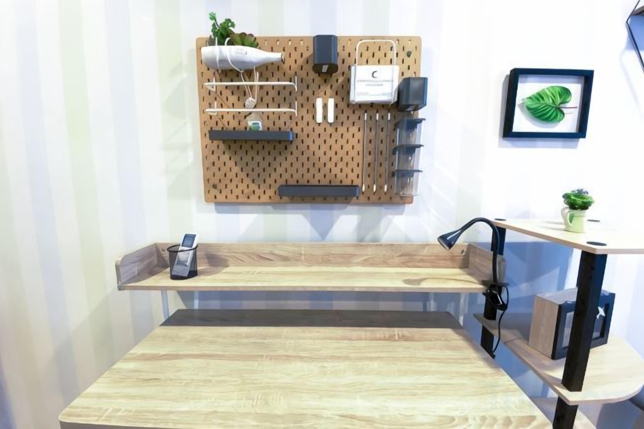 A room with a wooden table, a pegboard wall with various items, a small shelf, and a plant.