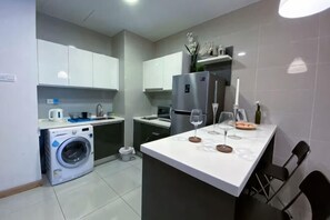 A modern kitchen with a washing machine, a refrigerator, a dining area with chairs, and a small island with a wine glass and a bottle. - KL Gateway Residence (Kuala Lumpur)