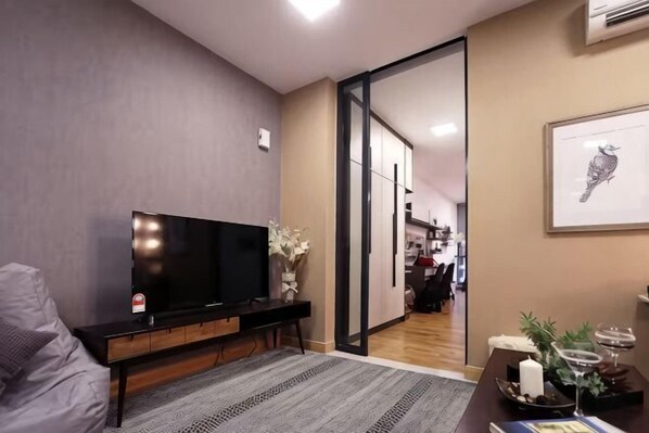 A modern living room with a flat-screen TV, a sofa, a coffee table, and a dining area with a candle and decorative items. - KL Gateway Residence (Kuala Lumpur)