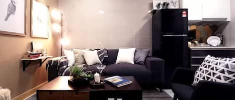Un espacio habitable compacto con sofá, una mesita de centro, área de cocina y refrigerador.