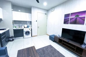 A compact living space with a kitchenette, a washing machine, a flat-screen TV, and a sofa. - KL Gateway Residence (Kuala Lumpur)
