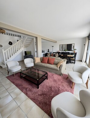 A living room with a sofa, chairs, a coffee table, a staircase, and a dining area.