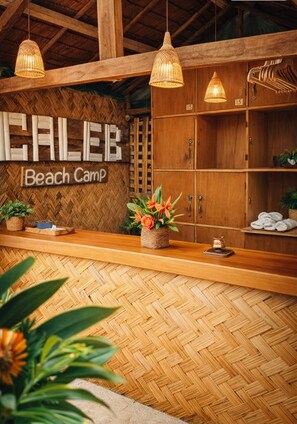 A reception area with a wooden counter, wicker pendant lights, and a sign that reads 'CALEB Beach Camp'. - Amwani Beach Camp (El Nido)