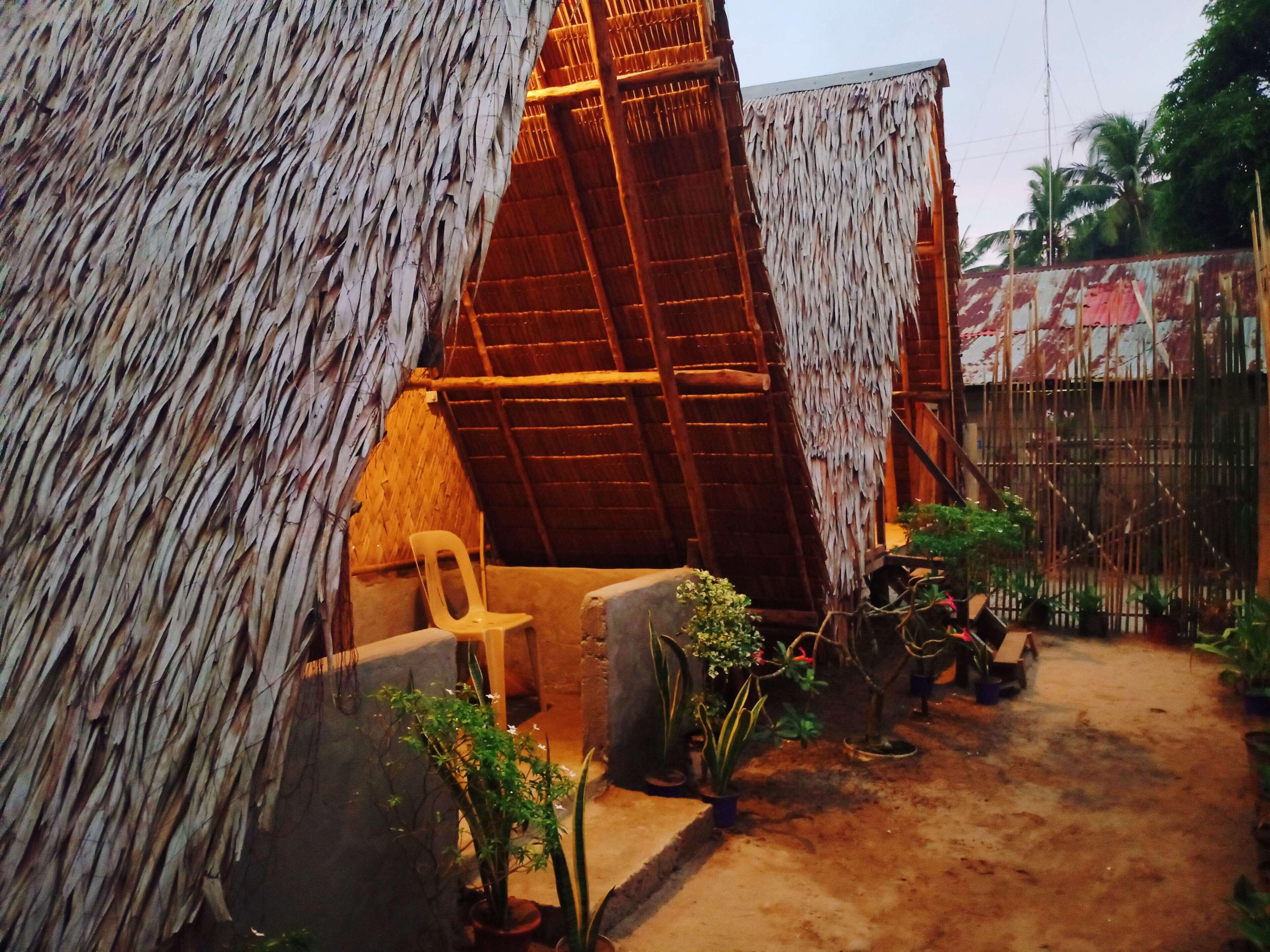 A thatched-roof structure with a wooden ladder and a plastic chair inside.