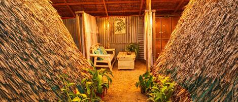 A rustic interior with thatched walls, a wooden bench, and potted plants.