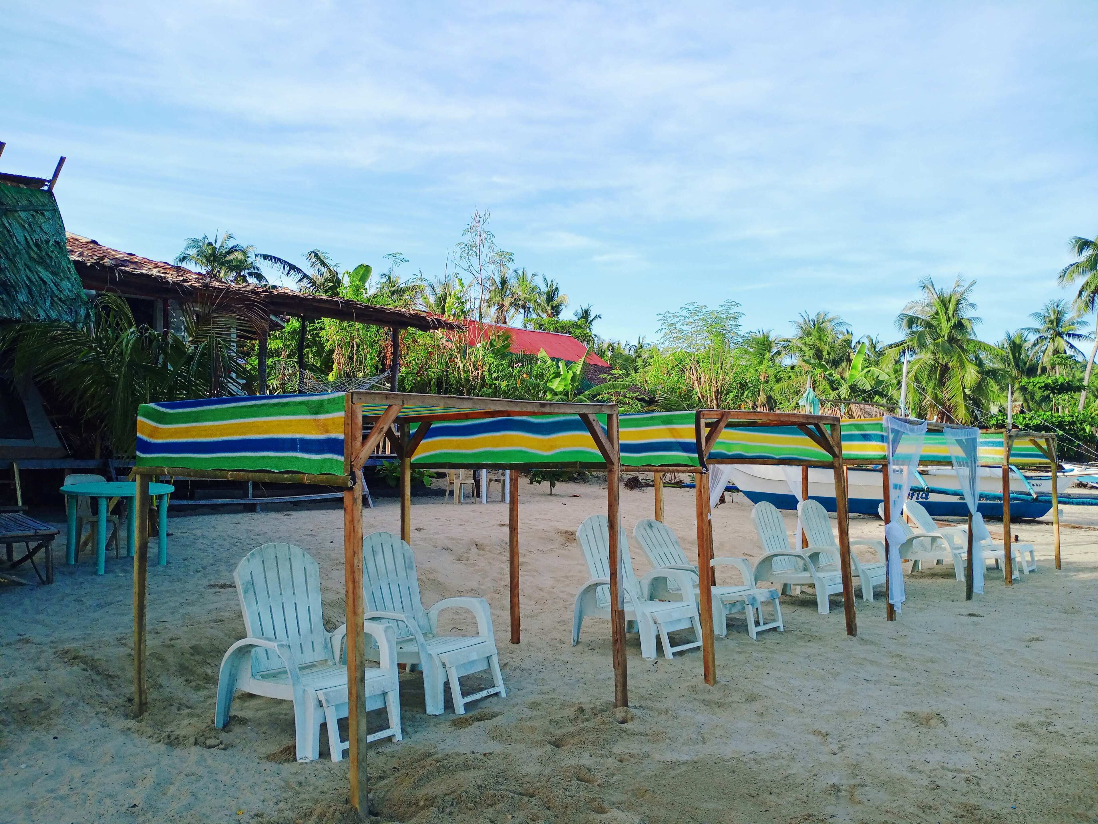 Un espacio de descanso frente al mar con sillas de plástico blanco y sombrillas a rayas.