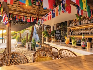 An outdoor bar area with wicker chairs, a thatched roof, and a variety of flags. - Amwani Beach Camp (El Nido)